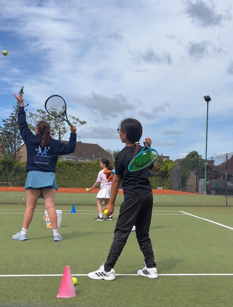 A Headstone coach demonstrating a serve to juniors during a group coaching session