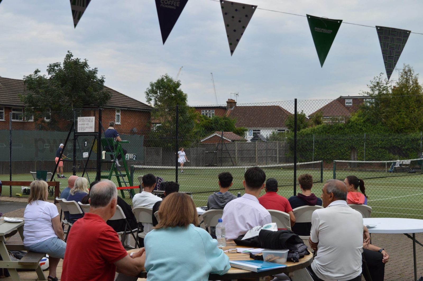 A match on court one at Headstone Tennis Club on finals day, watched from tables under bunting